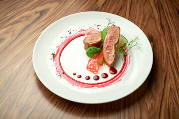 Duck fillet with baked vegetables and red sauce in a white plate on a wooden background