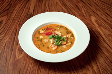 Asian soup tom yam with shrimps and chicken in a white plate on a wooden background