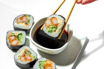 Hand dipping sushi roll with shrimp in soy sauce on white plate