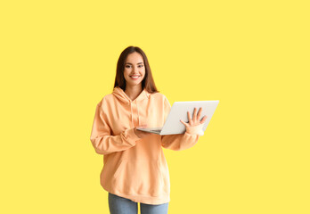 Beautiful young woman in stylish hoodie and with laptop on color background