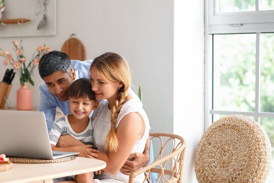 Happy parents with their little son using laptop at table in kitchen - Powered by Adobe