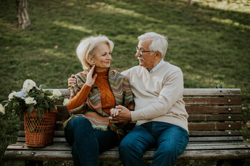 Senior couple sitting on the benchwith basket full of flowers and embracing