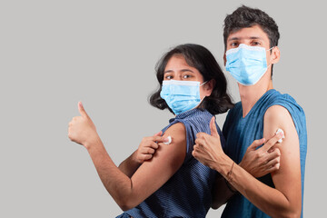 Young Latin couple recently vaccinated, wearing mask, isolated on plain background.