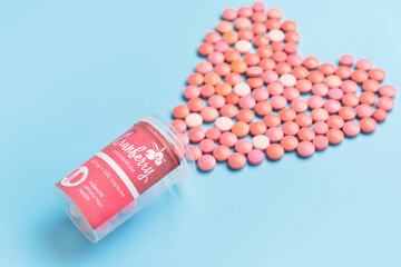 Heart made of cranberry pills on color background