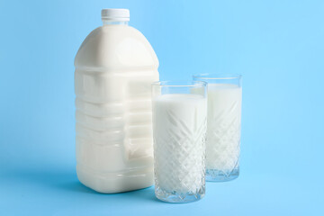 Gallon bottle and glasses of milk on blue background