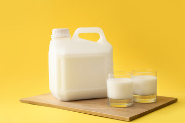 Board with gallon bottle and glasses of milk on yellow background