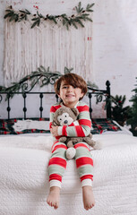 boy playing on a bed with his teddy bear and christmas pajamas 