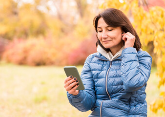 Happy woman through mobile phone and headphones listening to favorite music in the park