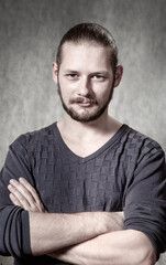 Portrait of serious young bearded man with mustache  on a gray background with folded his hands and fixedly looks