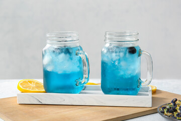 Mason jars of iced blue tea with lemon on light background