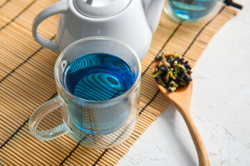 Glass cup of organic blue tea and dried flowers on light background, closeup