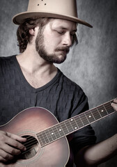 A charismatic man with a beard, playing an acoustic guitar, on a gray  background