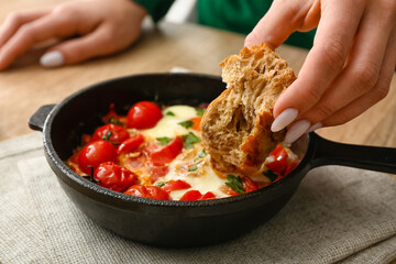 Woman eating tasty Shakshouka at table