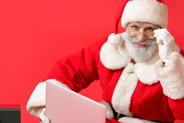 Santa Claus with modern laptop on color background