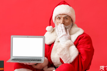 Surprised Santa Claus with laptop on color background