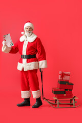 Santa Claus with letter and gifts on sledge against color background