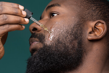African bearded man with pimples  applying oil on his skin