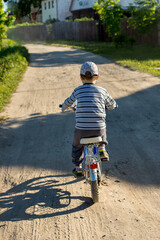 Child rides a two-wheeled bike on a country road. Little boy learning to ride a bicycle without training wheels. Active outdoor sport for kids on a summer day . Children cycling.