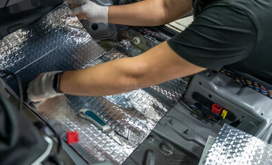 Worker hands glues soundproofing material to inside of car floor. Process of car sound insulation...