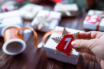 Obraz premium Hand tying packing tape around gift box for advent calendar. Making a calendar to prepare for Christmas. Decorating gifts. Tag with the number 24, the day before Christmas on a wooden table