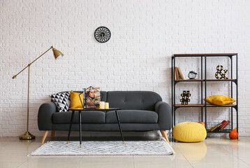 Interior of light room with floor lamp, sofa, shelf unit, table with magazines and candles