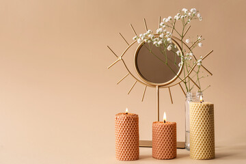 Burning candles, mirror and gypsophila flowers on beige background