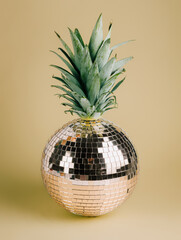 Golden shiny disco ball with pineapple leaves on the top isolated on beige background. Christmas...