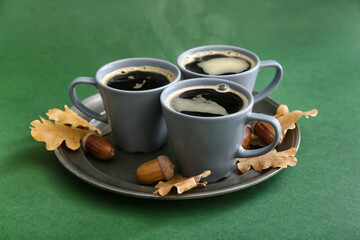Cups of coffee with acorns and autumn leaves on green background