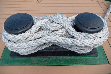 A black paired vertical metal bitts posts with a thick ship rope twisted on it, installed on board...