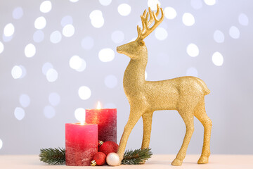 Golden reindeer, fir tree branches, Christmas balls and burning candles on table against light background