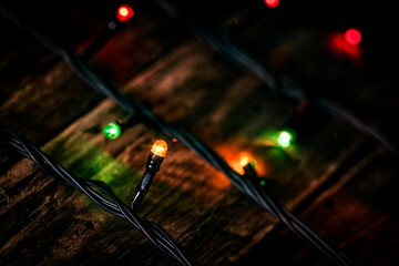 christmas garland of colorful light bulbs on an dark old weathered vintage table or wooden brown board. Christmas decoration, New Years Eve. Selective focus, bokeh, space for text.