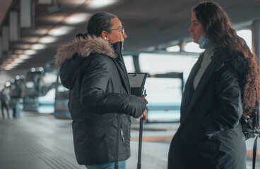 Viajeras de empresa de cabello oscuro observando impacientes de pie esperando con su mochila y maletas de viaje en la estación de autobuses junto sus papeles para tomar su trayecto de transporte