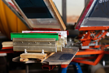 squeegees on wooden shelve of the print screening apparatus. serigraphy production. printing images on t-shirts by silk screen method in a design studio