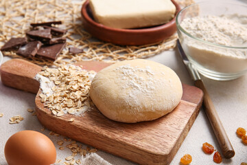 Wooden board with fresh dough and ingredients for preparing homemade cookies on light background