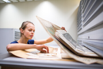 Pretty, young woman studying old maps in archives