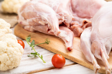 Whole raw rabbit with cauliflower, tomatoes and spices on a white wooden background. Side view, selective focus.
