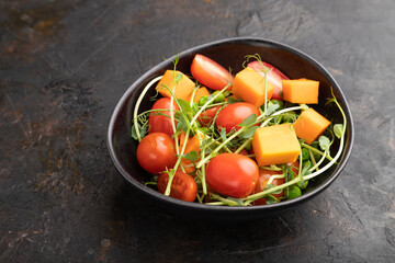 Vegetarian vegetable salad of tomatoes, pumpkin, microgreen pea sprouts on black concrete background. Side view, copy space.