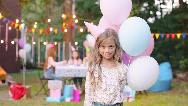 Close up of the caucasian little cute girl in a conus standing with balloons and smiling while celebrating her birthday. Portrait
