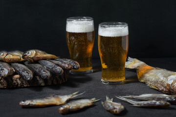 Fish, ready-made, dry, salted, many, different varieties are laid out on a dark background with beer poured into glasses with foam. Guster, taranka, roach, pike perch