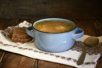 Homemade soup with meatballs in a ceramic bowl with a kitchen napkin on a kitchen wooden table, bread and a spoon.