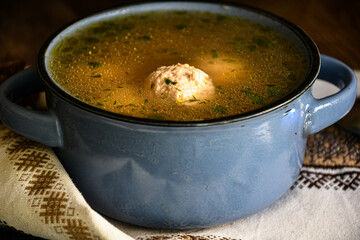 Homemade soup with meatballs in a ceramic bowl with a kitchen napkin on a kitchen wooden table, bread and a spoon.