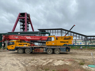A large yellow truck crane stands ready to work on the construction site of the new plant