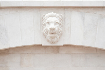 The face of a lion is made of white stone. A decorative element in the interior of a stone white wall