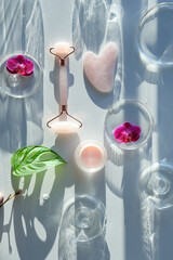 Pink quartz face roller and guasha stone. Exotic monstera leaves, orchid flowers, petri dishes and...
