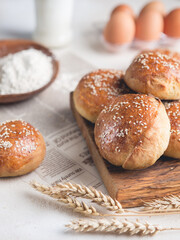 Group of tasty buns with sesam for burgers on wooden cutting board and ingredients on white table