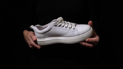 Hands holding white leather sneaker with laces against black background