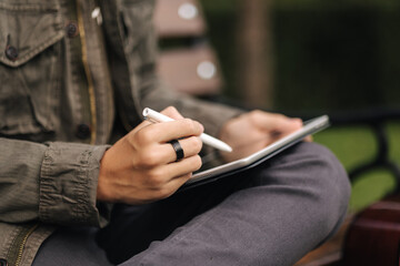 Close-up of boy painting in tablet using pencil. Young designer using tablet outdoor. Autumn time