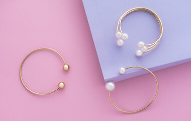 Top view of golden bracelets with pearls on pink and purple paper background with copy space