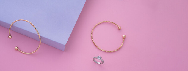 Panoramic shot of modern golden bracelets and ring on pink and purple
