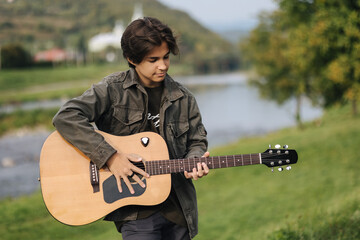 Concentrated teenage boy musician playing acoustic guitar outdoor. Handsome boy love misuc